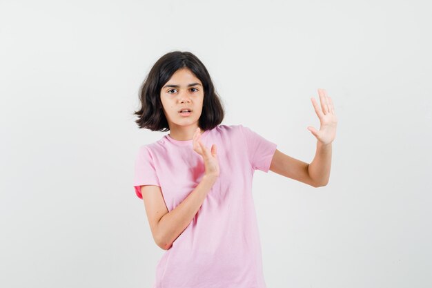 Little girl keeping hands to defend herself in pink t-shirt and looking scared , front view.