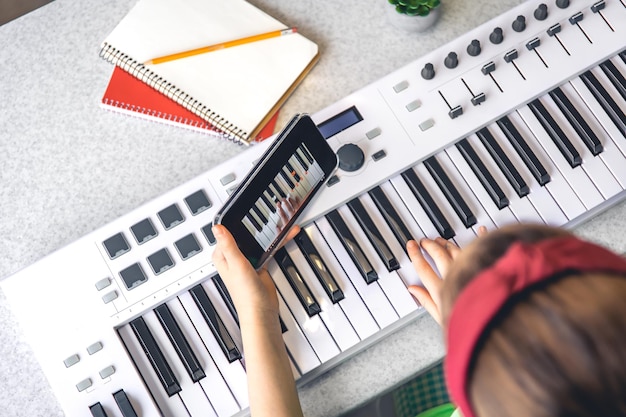 Free photo a little girl learns to play the piano with a smartphone online music lesson