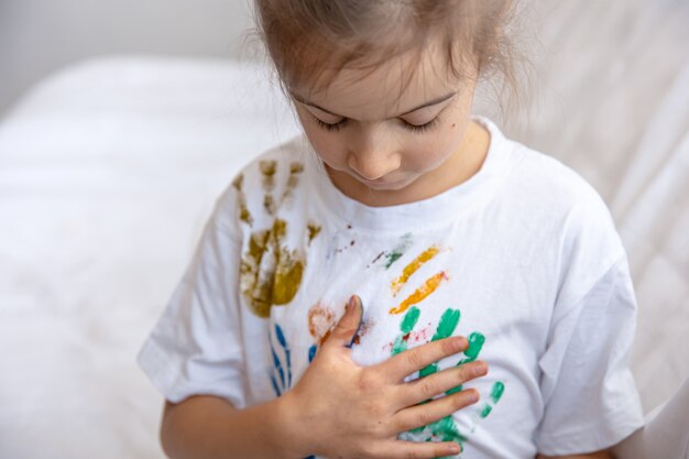 A little girl leaves traces of painted palms on a T-shirt. Children's creativity and art.