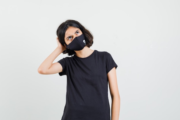 Free Photo little girl looking up in black t-shirt, mask and looking pensive , front view.