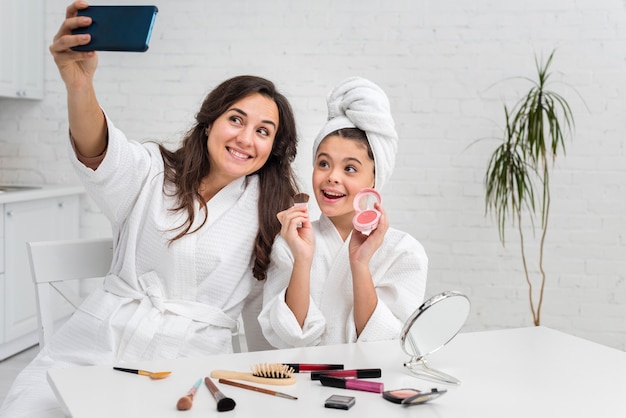 Free photo little girl and mother taking a selfie while doing their make-up