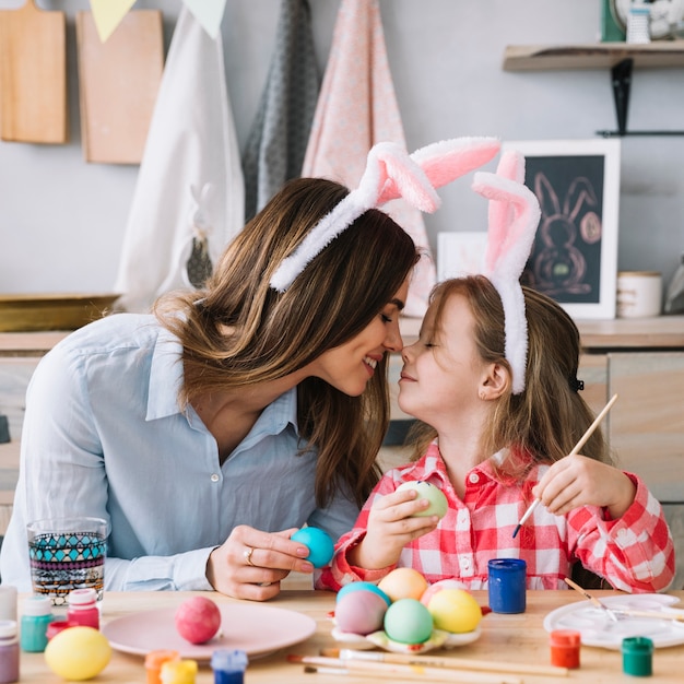 Free Photo little girl and mother touching noses while painting eggs for easter