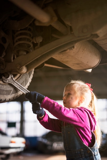 Little girl in overall repairing car with spanner 