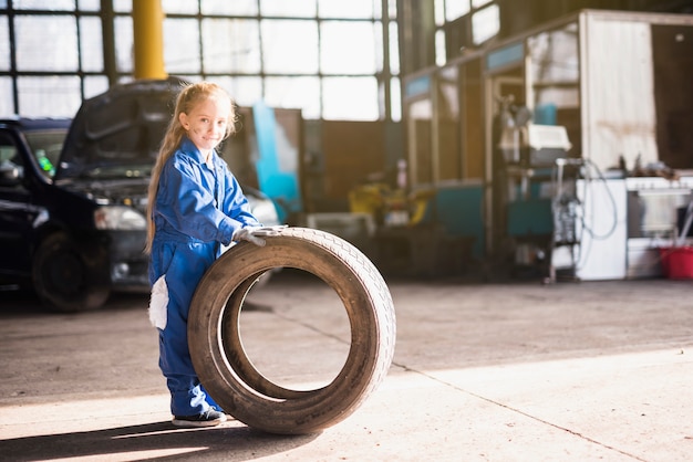 Little girl in overall standing with car wheel 