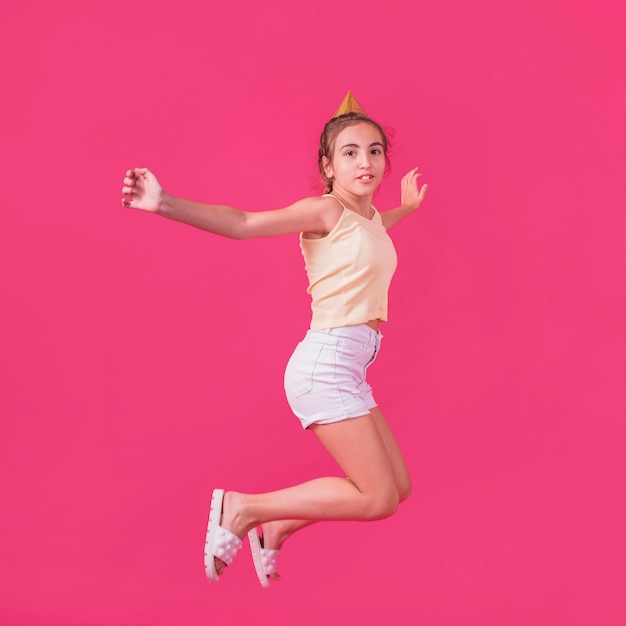 Free Photo little girl in party hat jumping on pink backdrop