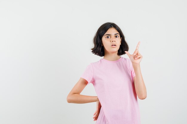 Little girl in pink t-shirt pointing up and looking anxious , front view.