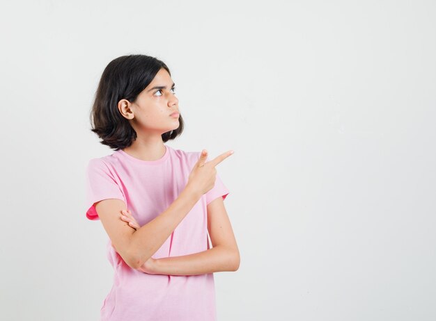 Little girl in pink t-shirt pointing at upper right corner and looking focused , front view.