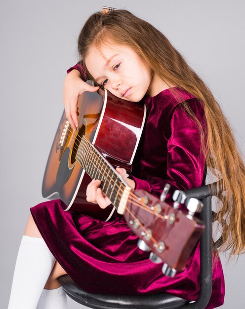 Little girl playing acoustic guitar on chair 