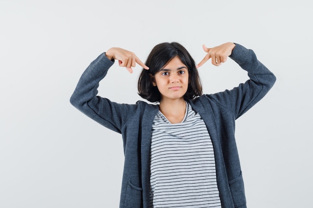 Little girl pointing at herself in t-shirt, jacket and looking proud.