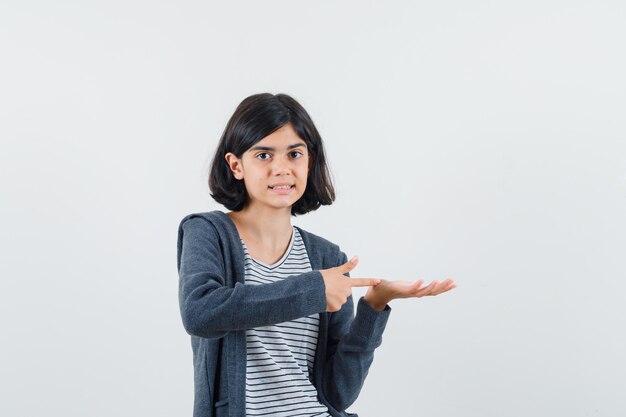 Little girl pointing at something pretended to be held in t-shirt, jacket and looking confident