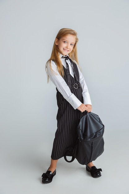 Free Photo little girl posing in school's uniform with backpack on white wall