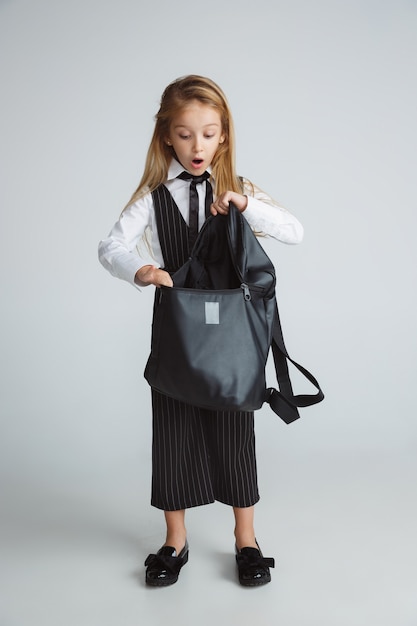 Free photo little girl posing in school's uniform with backpack on white wall