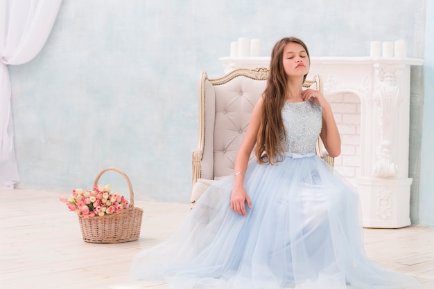 Free photo little girl posing while sitting on arm chair near flower basket