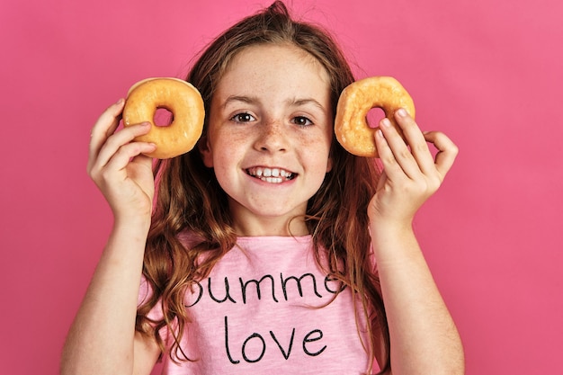 Little girl posing with a couple of donuts on a pink