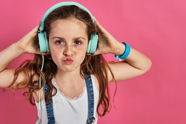 Little girl posing with headphones on a pink wall