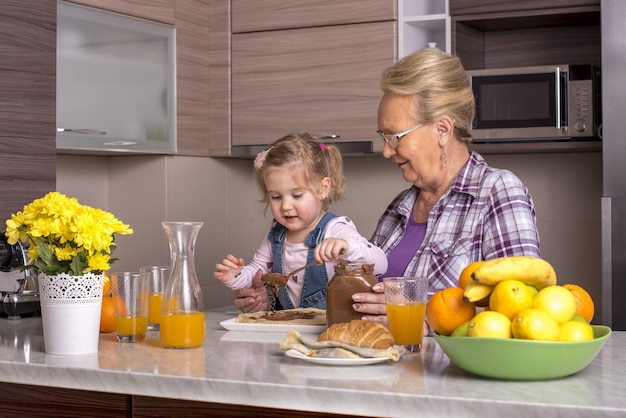 Little girl preparing pancakes with chocolate cream in the kitchen with her grandmother