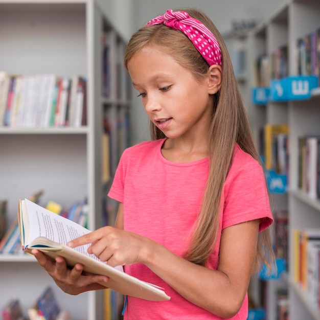 Free photo little girl reading a book in the library