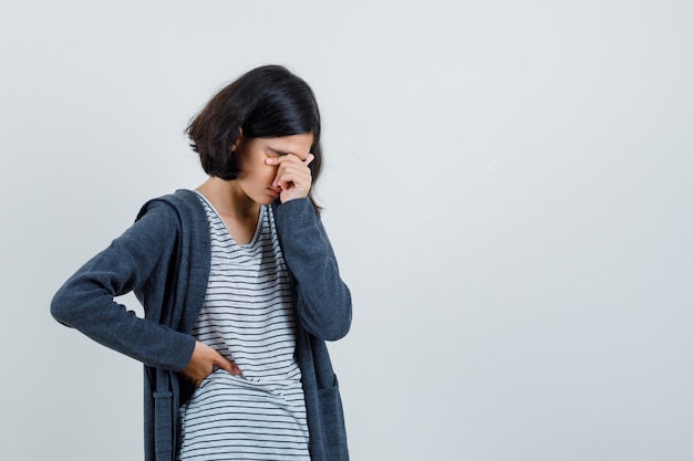 Little girl rubbing eyes and nose in t-shirt, jacket and looking fatigued