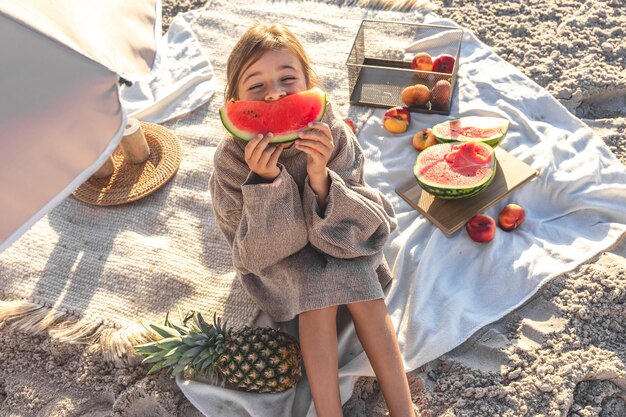 A little girl on a sandy sea beach eats a watermelon