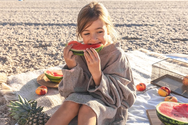 A little girl on a sandy sea beach eats a watermelon