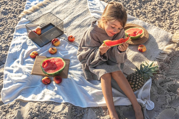 A little girl on a sandy sea beach eats a watermelon