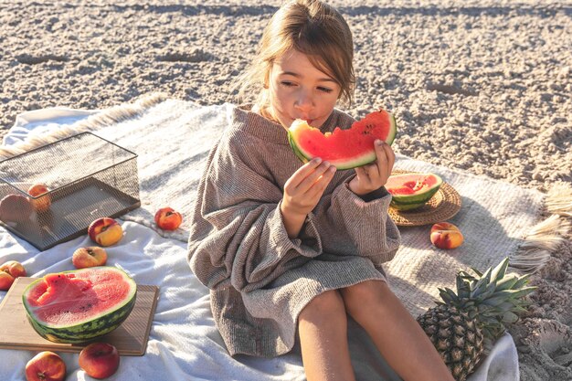 A little girl on a sandy sea beach eats a watermelon