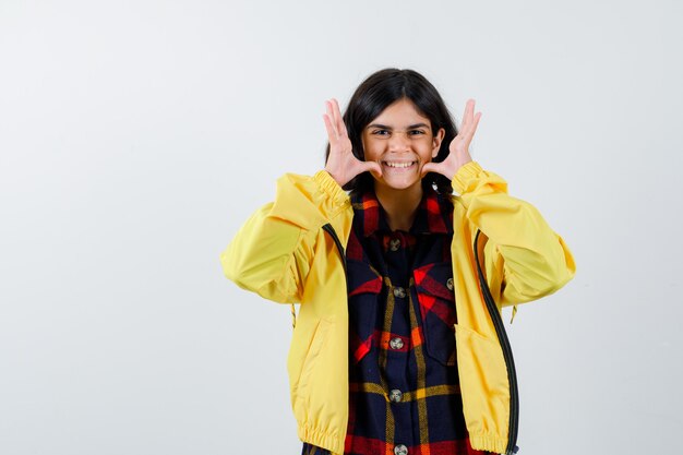 Little girl showing funny gesture in checked shirt, jacket and looking cute 