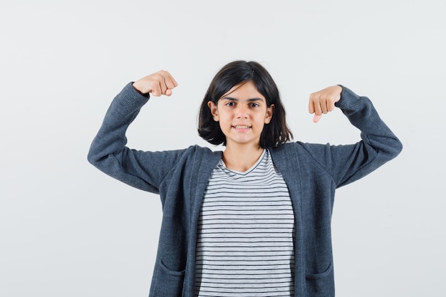 Little girl showing muscles of arms in t-shirt, jacket and looking confident.