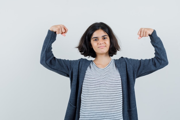 Little girl showing muscles of arms in t-shirt, jacket and looking confident