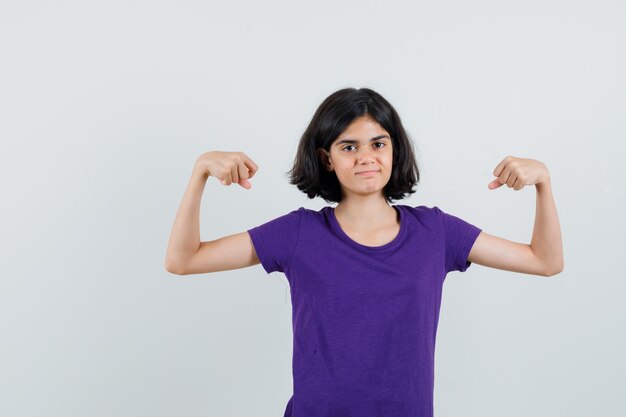 Little girl showing muscles of arms in t-shirt and looking confident.