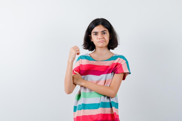 Little girl showing power gesture in t-shirt and looking displeased. front view.