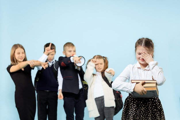 Little girl sitting alone on chair and suffering an act of bullying while children mocking