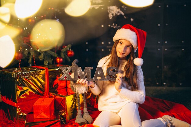 Little girl sitting by christmas tree and unpacking presents