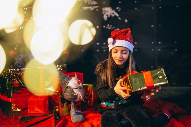 Free photo little girl sitting by christmas tree and unpacking presents