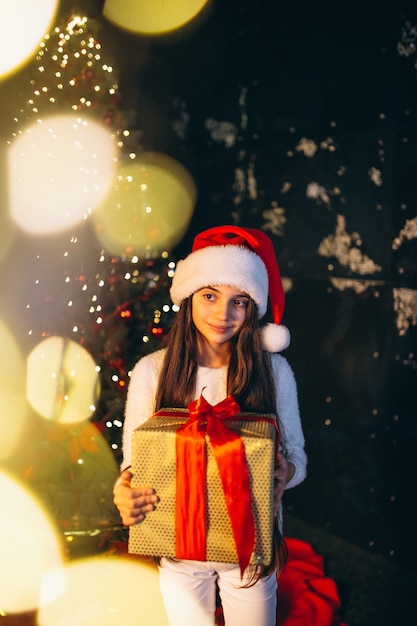 Little girl sitting by christmas tree and unpacking presents