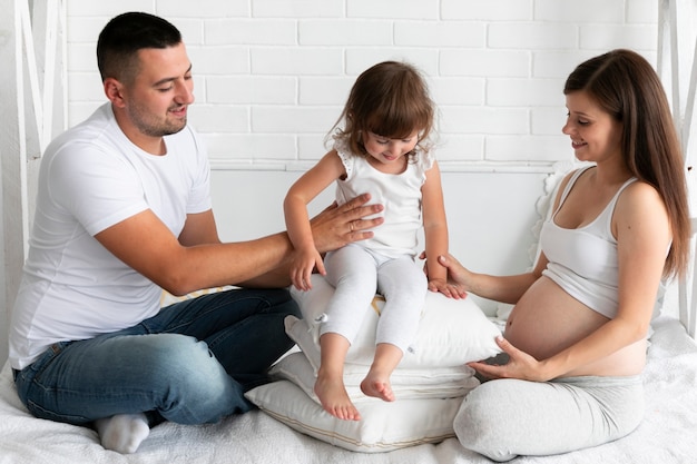 Free photo little girl sitting on pillows next to parents