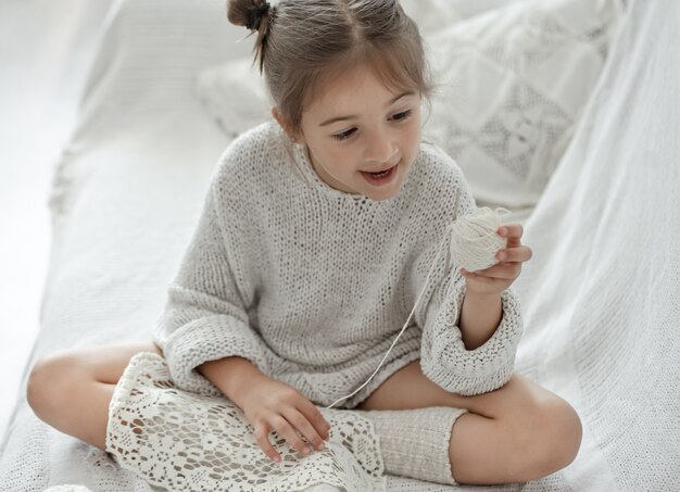 Little girl sitting on the sofa and learning to knit, home leisure concept.