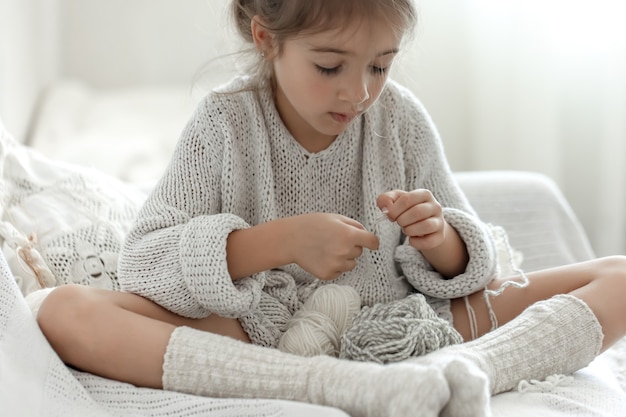 Little girl sitting on the sofa and learning to knit, home leisure concept.