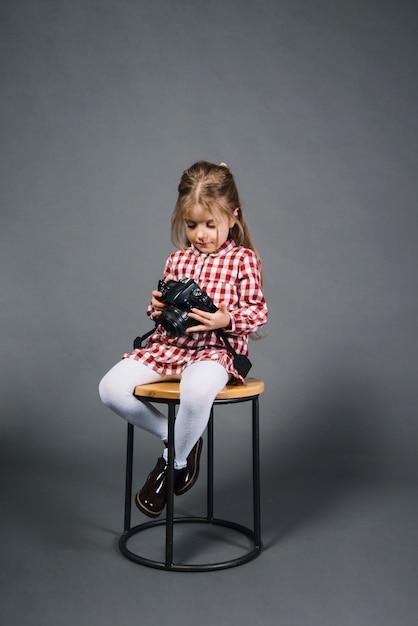 Little girl sitting on stool looking at camera against gray background