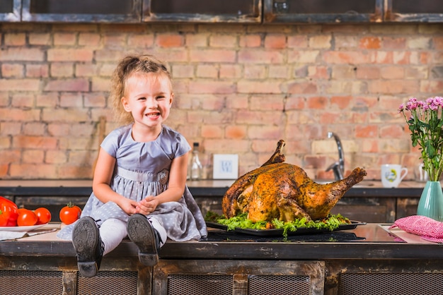 Little girl sitting on table with roasted turkey