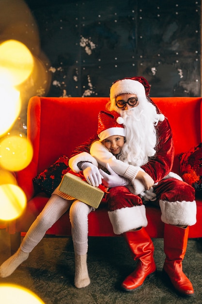 Free photo little girl sitting with santa and presents on christmas