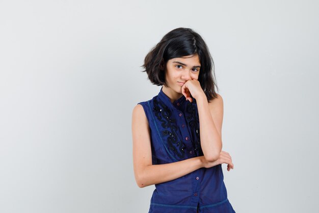 Little girl standing in thinking pose in blue blouse and looking ashamed.