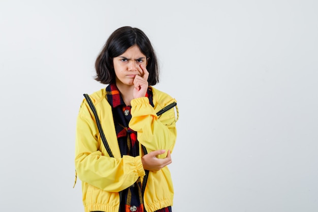 Little girl standing in thinking pose in checked shirt, jacket and looking thoughtful