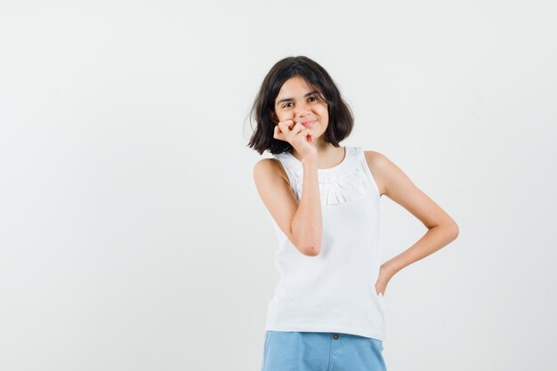 Little girl standing in thinking pose in white blouse, shorts and looking nice , front view.