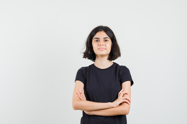 Little girl standing with crossed arms in black t-shirt and looking confident. front view.