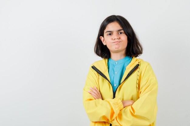 Little girl standing with crossed arms while blowing cheeks in shirt, jacket and looking confident , front view.