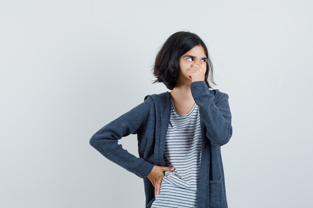 Little girl in t-shirt, jacket holding her nose and looking pensive ,