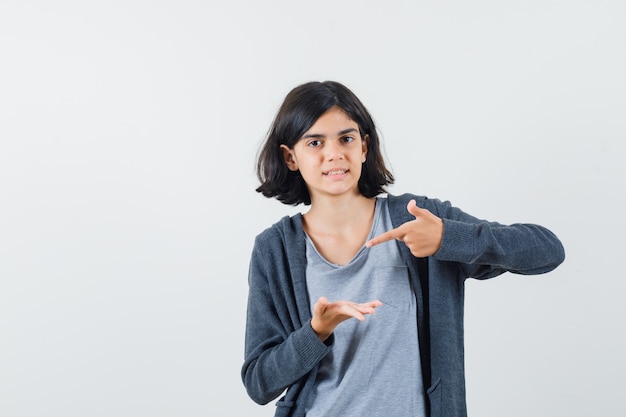 Little girl in t-shirt, jacket pointing at her palm and looking confident