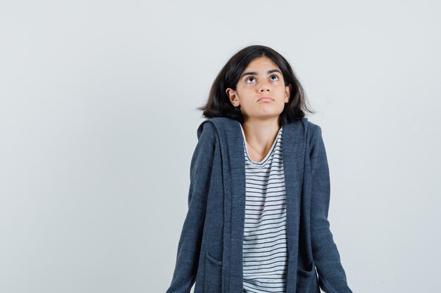 Little girl in t-shirt, jacket shrugging by looking up and looking confused ,