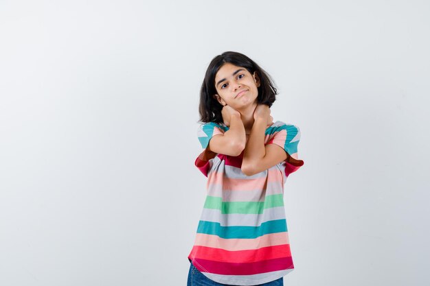 Little girl in t-shirt keeping hands on neck and looking cute , front view.